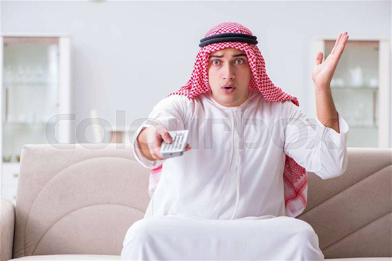 Arab man watching tv at home, stock photo