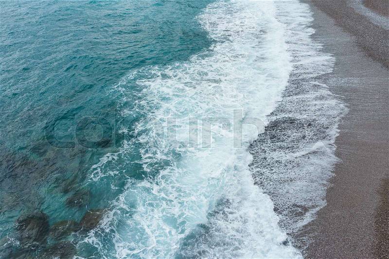 Soft and gentle blue sea waves foam in italy stone sand coast shore in summer daylight, stock photo