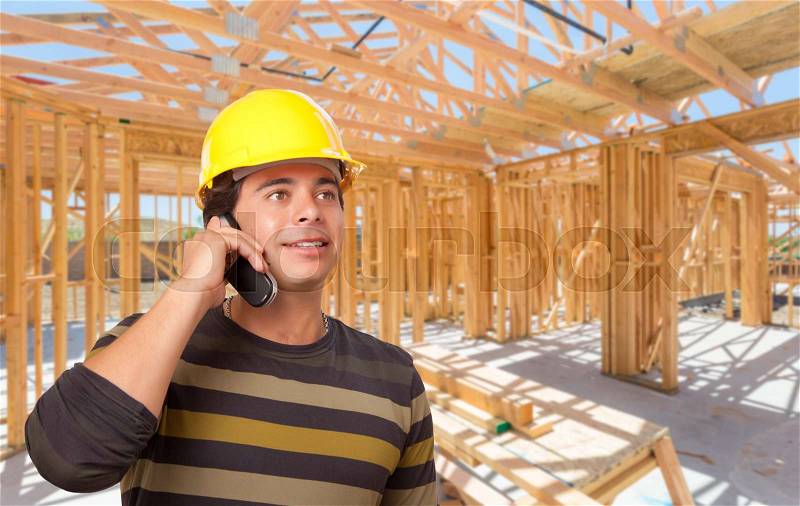 Hispanic Contractor Using Phone On Site Inside New Home Construction Framing, stock photo
