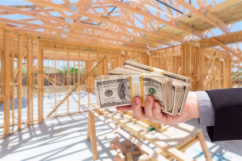 Hand With Stacks of Cash On Site Inside New Home Construction Framing, stock photo