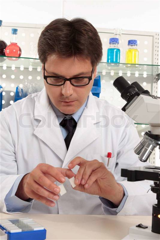 Scientist sitting at desk in a a laboratory using microscope slides, stock photo