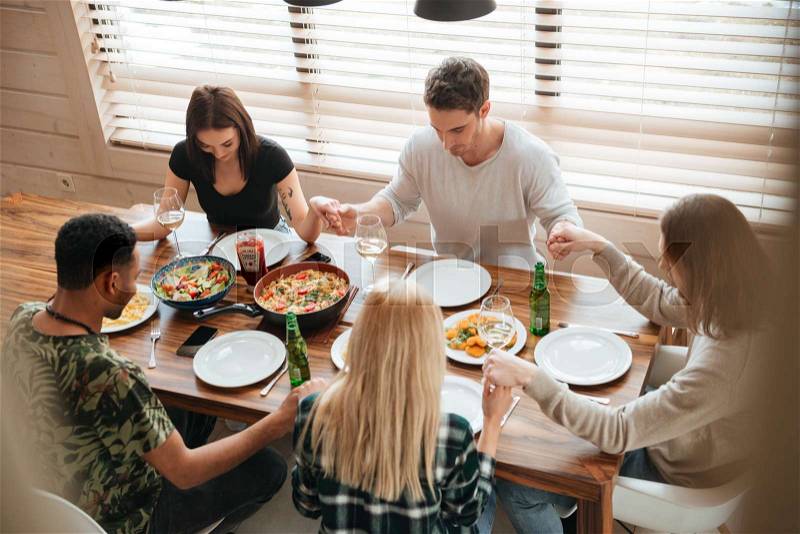 Group of peaceful young people holding hands and praying at the dinner table, stock photo