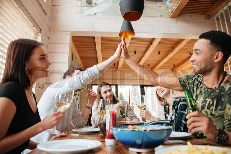 Group of people having dinner and giving high five at the table at home, stock photo