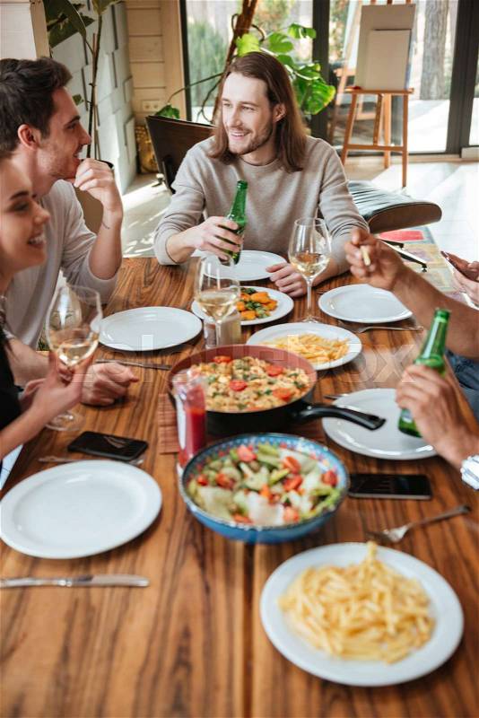 Group of cheerful young friends eating and talking at the table at home, stock photo
