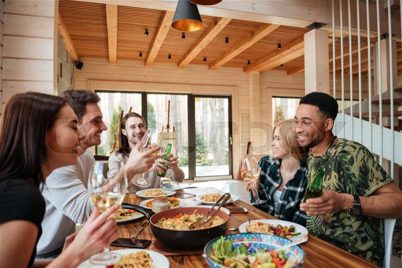 Group of cheerful young friends having dinner and laughing at the table at home, stock photo