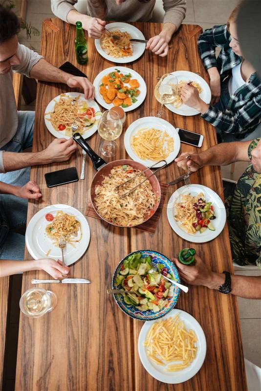 Top view of group of people having dinner together while sitting at the rustic wooden table at home, stock photo