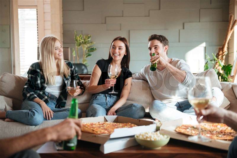 Group of cheerful young friends with pizza, wine and beer talking and having fun on sofa at home, stock photo
