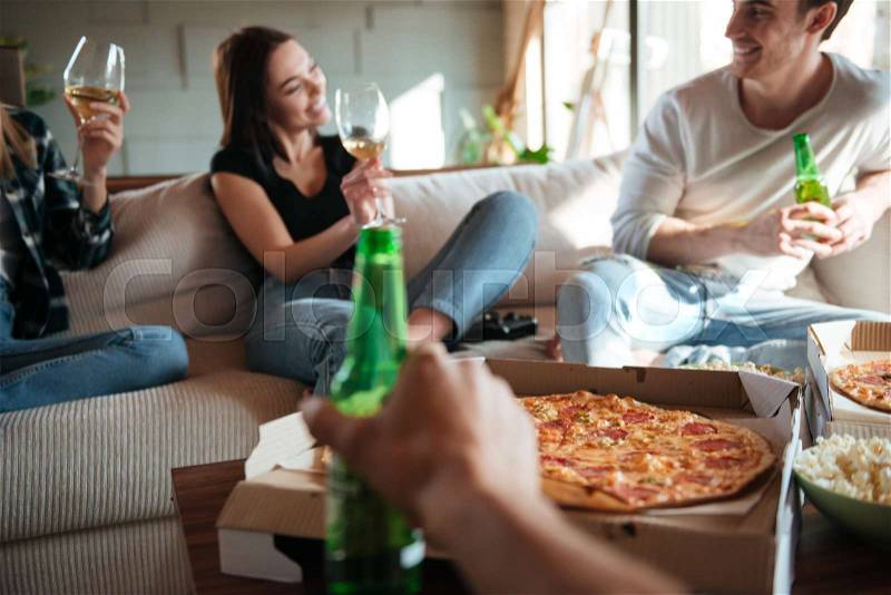 Group of cheerful young people with pizza, wine and beer talking and laughing on sofa at home, stock photo