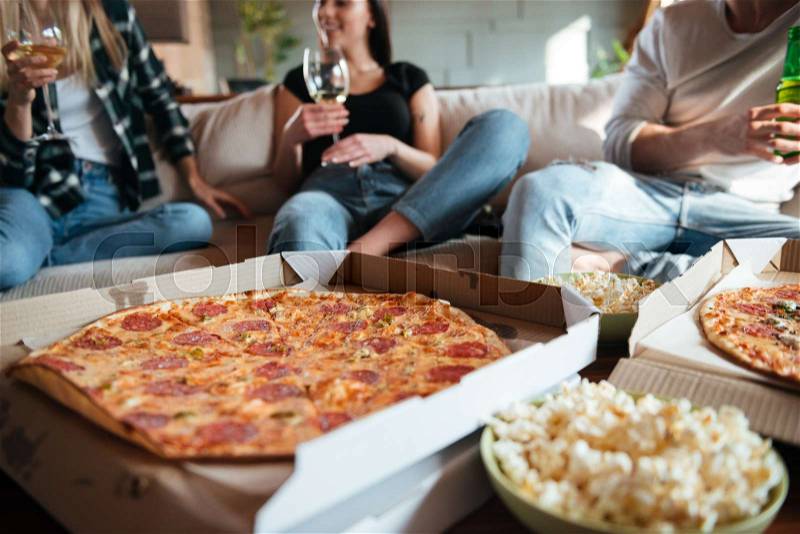 Group of happy young people eating pizza, drinking wine and beer on sofa at home, stock photo