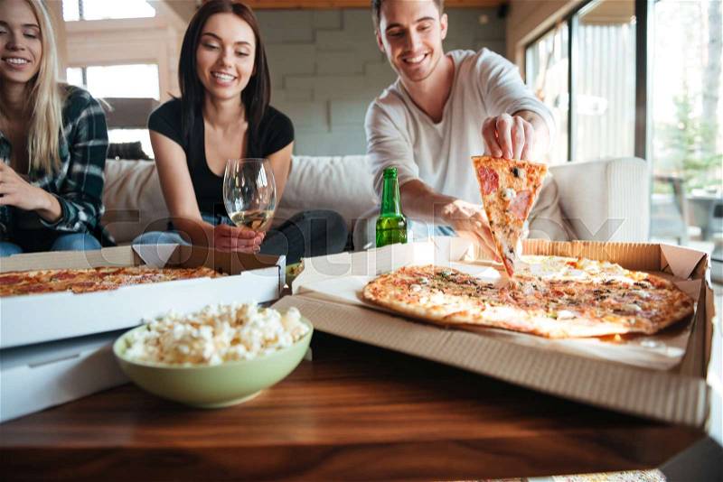 Group of young friends eating tasty pizza at home while having a party, stock photo