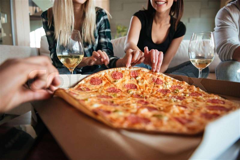 Cropped image of a group of friends eating big pizza and drinking white vine while having a home party, stock photo