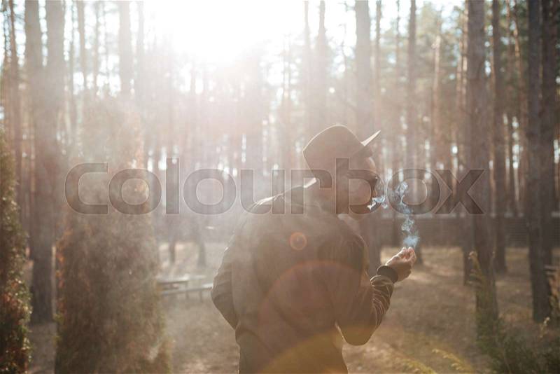 Back view image of african man standing outdoors in the forest smoking, stock photo