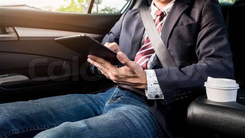 Young handsome businessman working in back of car and using a tablet or smart phone, stock photo