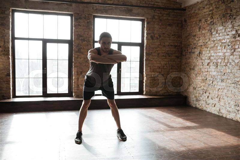 Full length portrait of a young healthy man in sportswear doing stretching exercises at the gym, stock photo