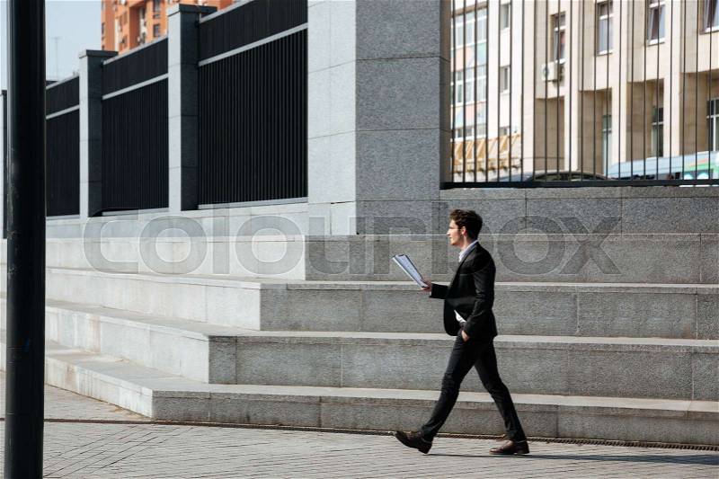 Full-length of businessman holding folder standing near stairs in the sreet, stock photo