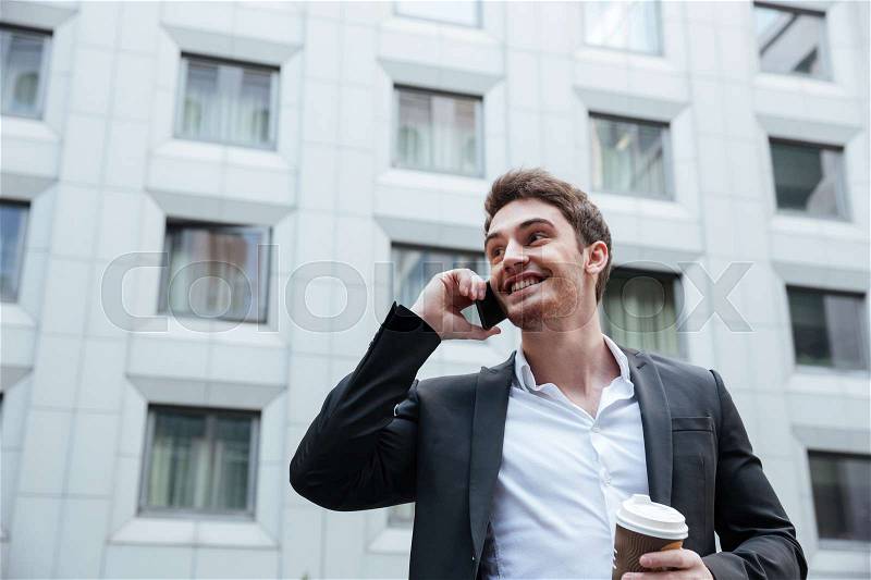 Young cheerful businessman talking on phone in business center, stock photo