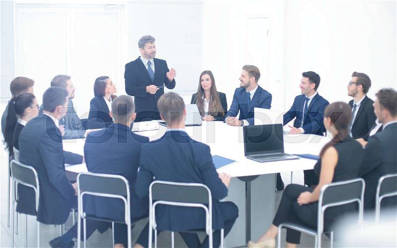 Heads of departments of the holding company at a meeting sitting at a round table and listening to the boss, who stands in the center and makes a report, stock photo