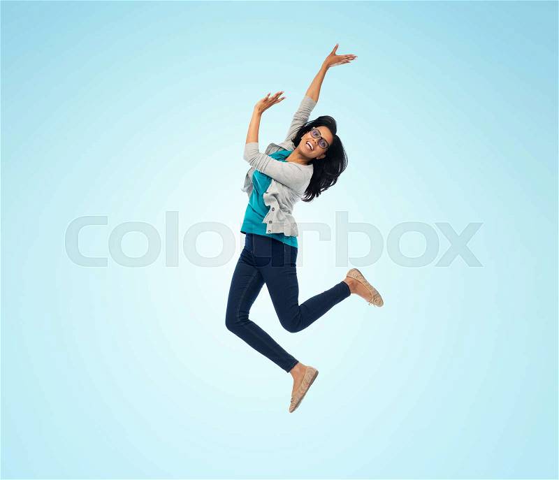 Freedom, motion and people concept - smiling young indian woman jumping in air over blue background, stock photo