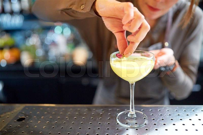 Alcohol drinks, people and luxury concept - woman bartender decorating cocktail in glass with dried flowers at bar, stock photo