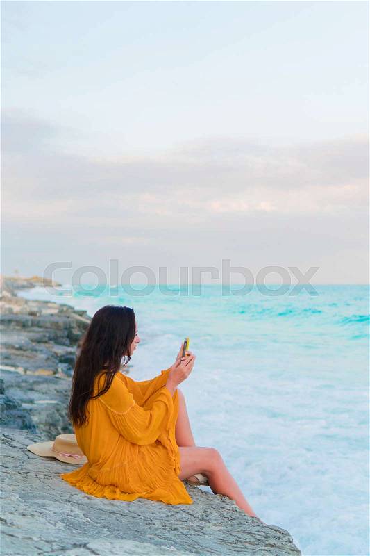 Young beautiful woman with cell phone in sunset. Happy girl in dress in the evening on the beach, stock photo