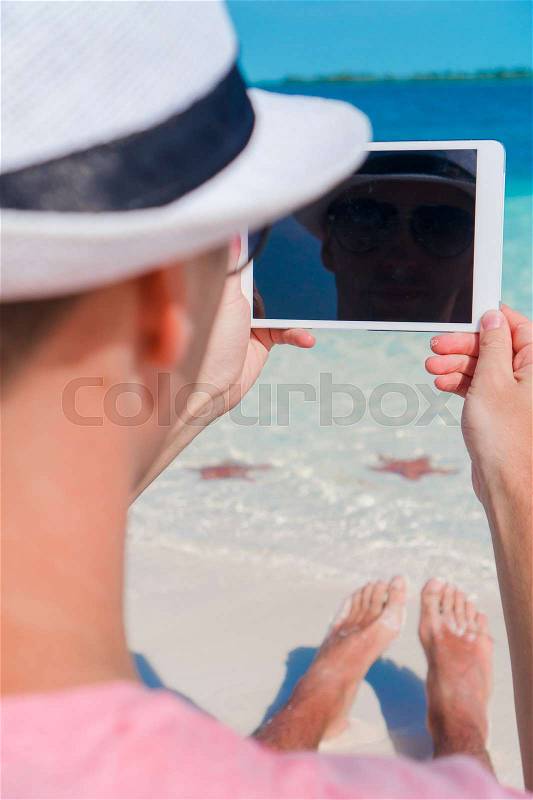 Young man with laptop on the background of turquoise ocean at tropical beach, stock photo