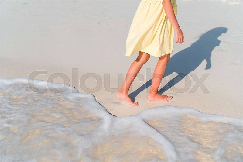 Closeup legs of little girl at shallow water on the beach, stock photo