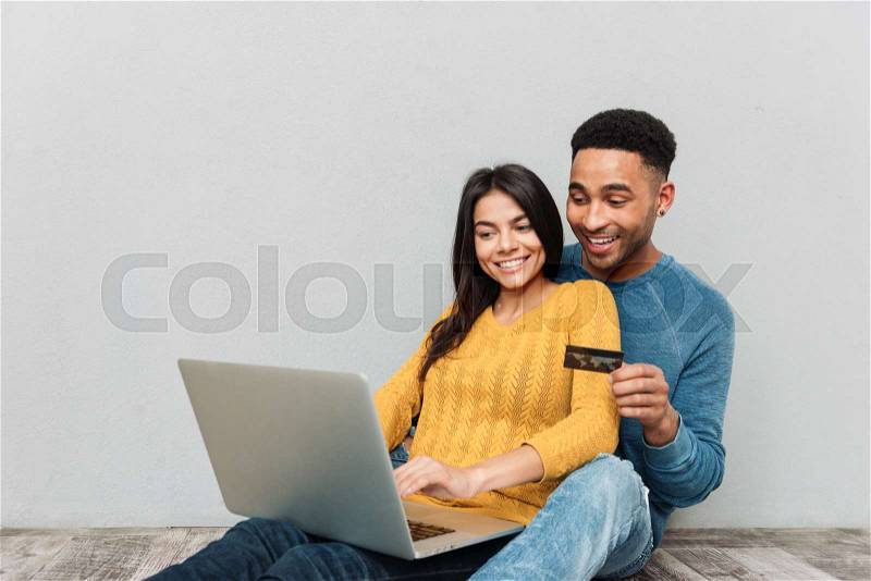 Smiling couple sitting on floor and using laptop and credit card for buying isolated, stock photo