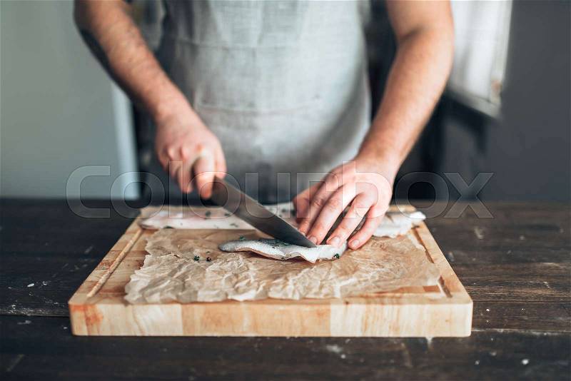 Male chef cuts with knife raw fish slices on wooden cutting board. Seafood cooking. Fresh sea food preparation, stock photo