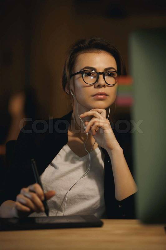 Woman designer listening music using headphones while working in office, stock photo
