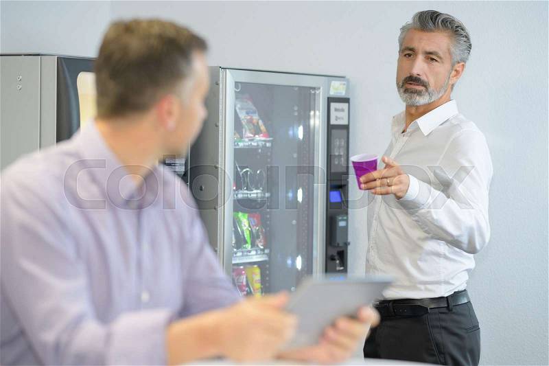 Businessman offering coffee from vending machine, stock photo