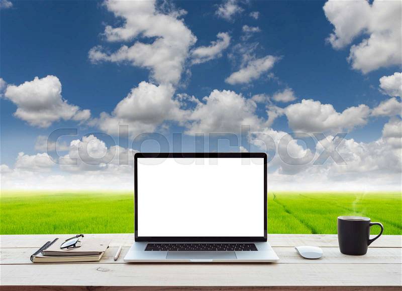 Laptop computer showing white screen on work table meadow and blue sky view background, stock photo