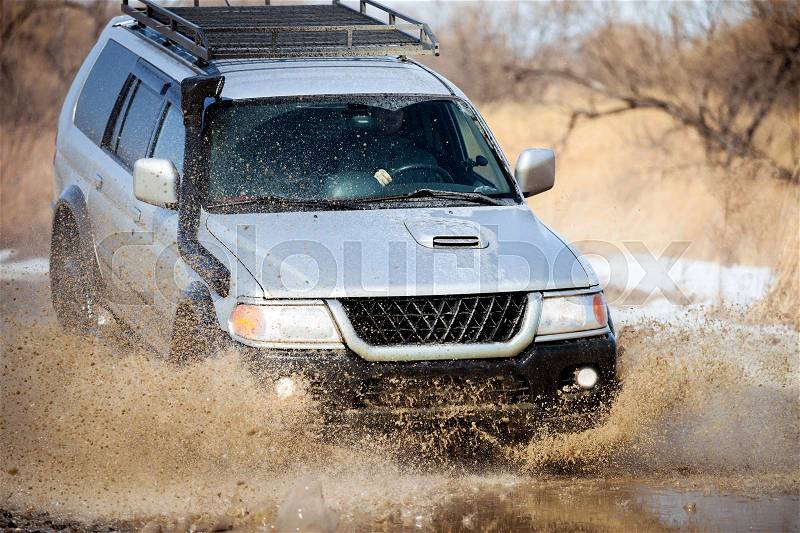 Mitsubishi Pajero Sport on dirt road in early spring making splashes from a big puddle, stock photo
