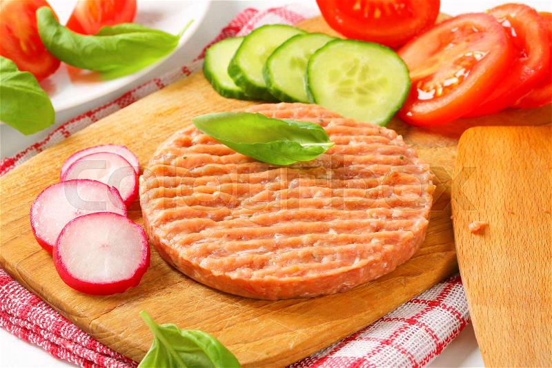 Raw burger patty and sliced vegetables on cutting board, stock photo