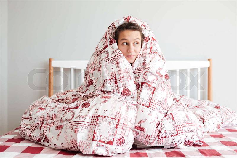 Young thoughtful woman wrapped in blanket in bedroom, stock photo