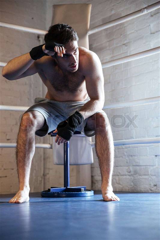 Tired boxer man wiping the sweat while sitting in the corner of boxing ring, stock photo