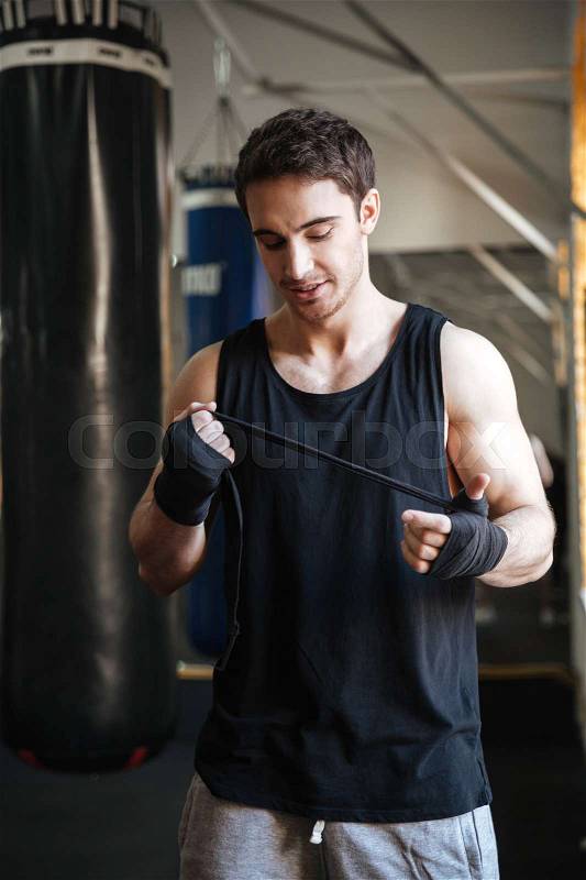 Smiling man standing near punching bag in gym and wearing boxing gloves, stock photo