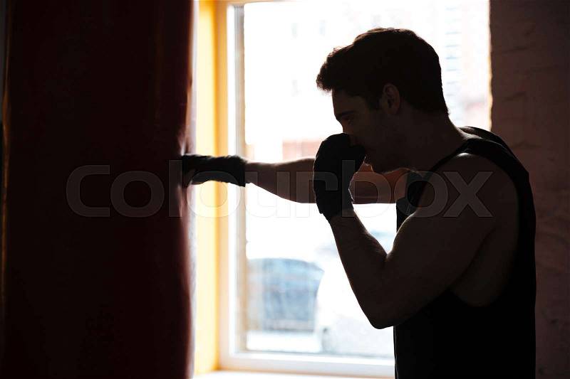 Young sportsman in shadow kicking the punching bag while training, stock photo