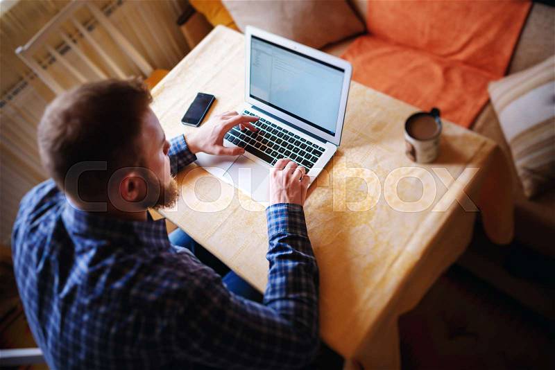 Surfing the net in office. Confident young man working on laptop and smiling while sitting at his working place in office, stock photo