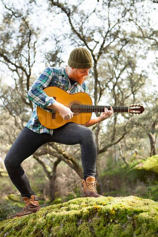 Guitarist with crazy face playing the guitar in the forest, stock photo
