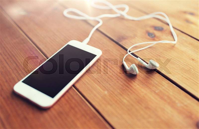 Technology, music, gadget and object concept - close up of white smartphone and earphones on wooden surface with copy space, stock photo
