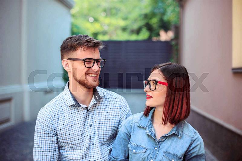 Happy funny couple standing outdoors at street of city and laughing on the bright sunny day and green summer background, stock photo