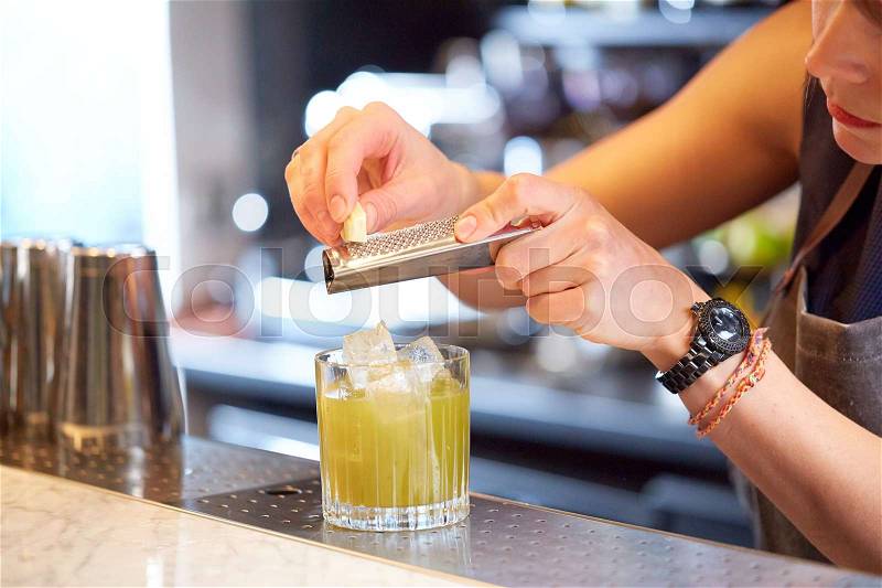 Alcohol drinks, people and luxury concept - close up of woman bartender with glass and grater grates white chocolate preparing cocktail at bar, stock photo