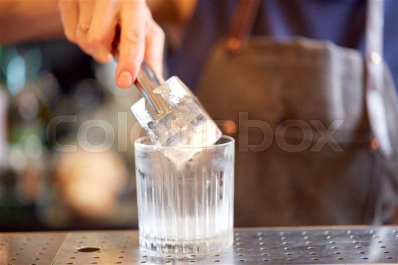 Alcohol drinks, people and luxury concept - bartender with tongs adding ice cube into glass and preparing cocktail at bar counter, stock photo