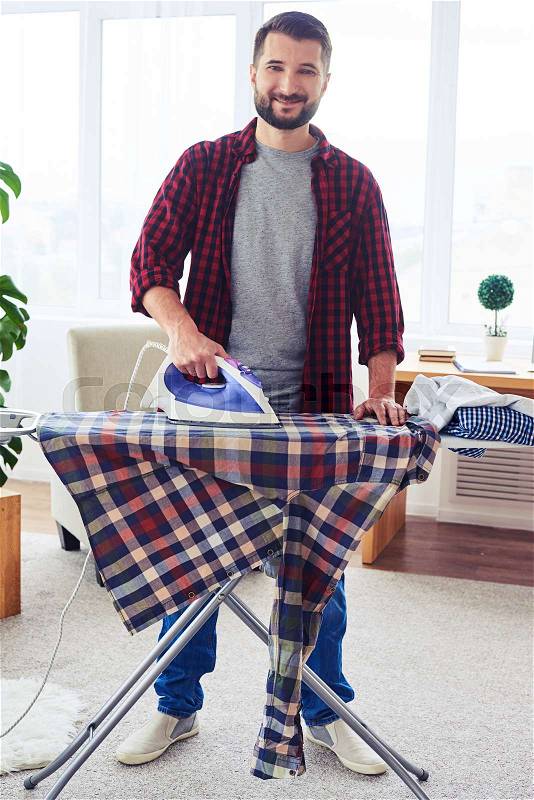Vertical of attractive male ironing clothes on ironing board, stock photo
