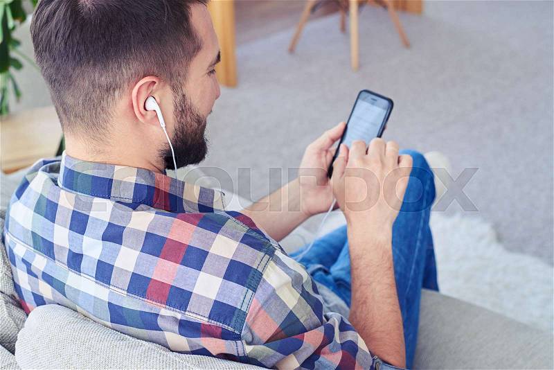 Close-up of bearded guy listening to music with headphones using smartphone, stock photo