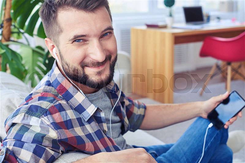 Close-up of guy with beautiful blue eyes listening to music with headphones and smiling, stock photo
