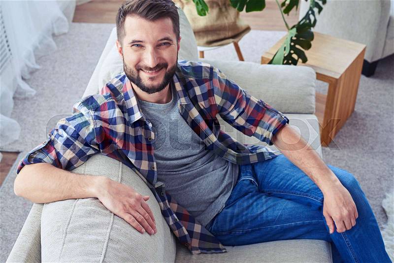 Mid shot of attractive man leaning on back oh sofa and having rest, stock photo