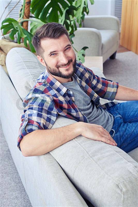 Vertical of gentleman with nice smile in checkered shirt leaning on back oh sofa and having rest, stock photo