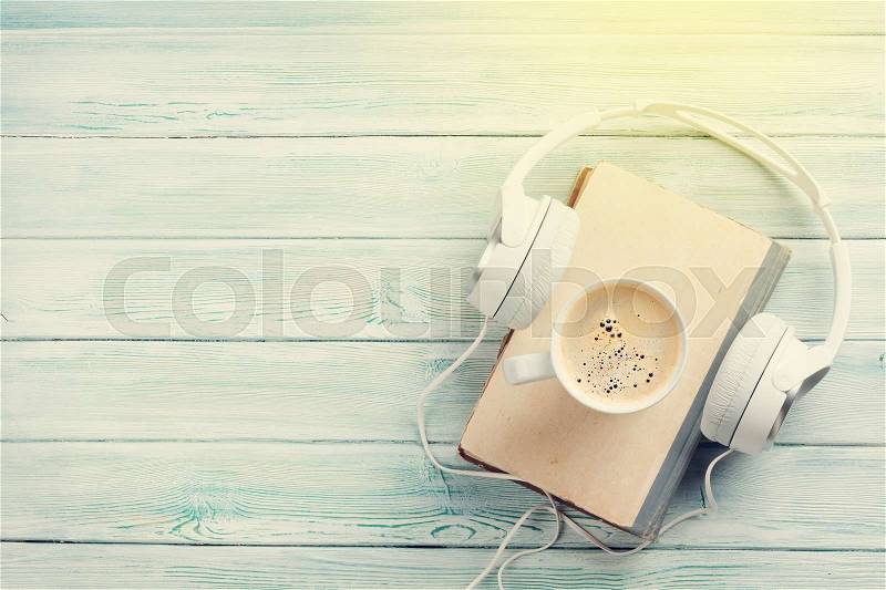 Audio book concept. Headphones, coffee and book over wooden table. Top view with space for your text. Sunny toned, stock photo