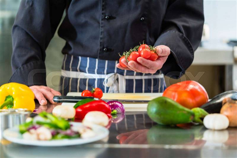 Chef cutting tomatoes for salad in hotel kitchen, stock photo
